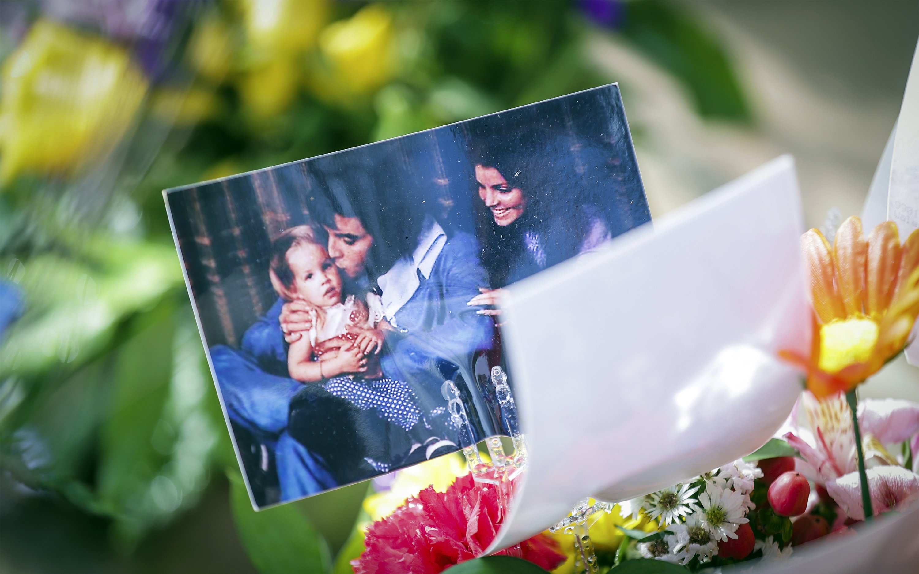 Foto Lisa Marie Presley muda bersama orang tuanya, Elvis Presley dan Priscilla Presley, duduk di atas karangan bunga selama upacara peringatan di Graceland di Memphis, Tenn., AS, 22 Januari 2023. (Foto AP)