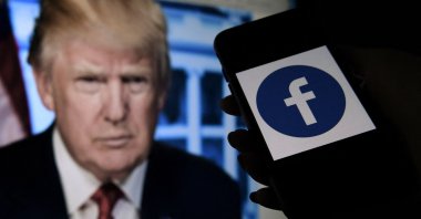 A phone screen displays a Facebook logo with the official portrait of former US President Donald Trump in the background in Arlington, Virginia, U.S., May 4, 2021. (AFP Photo)