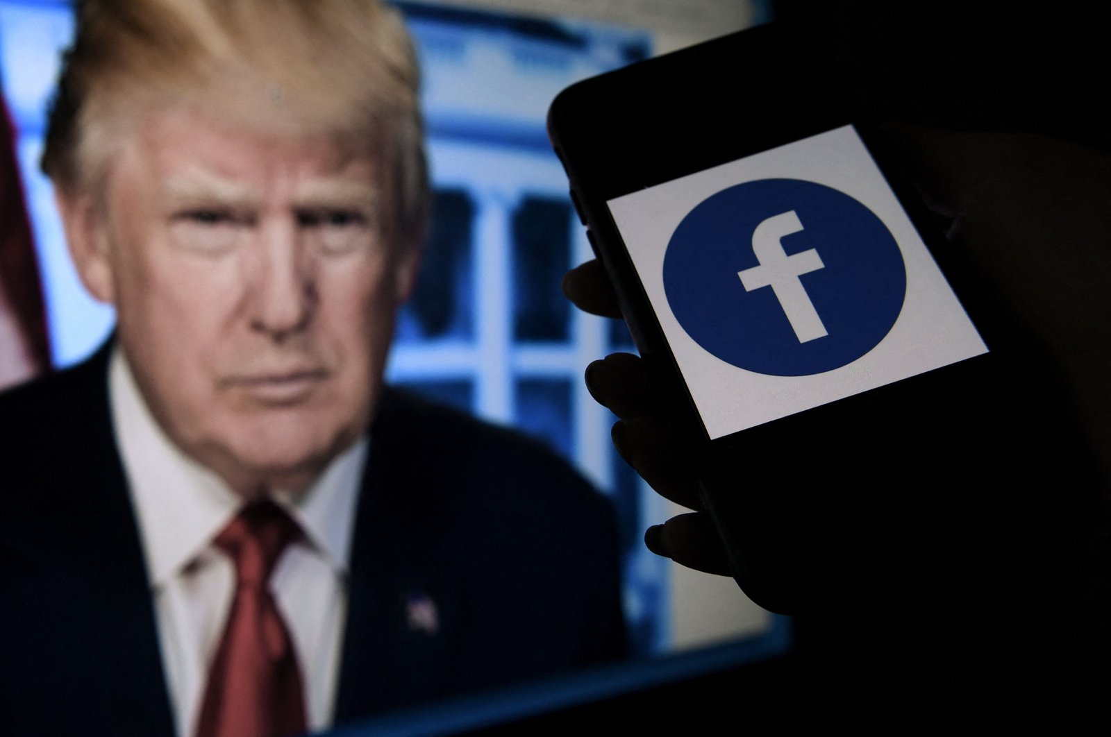 A phone screen displays a Facebook logo with the official portrait of former US President Donald Trump in the background in Arlington, Virginia, U.S., May 4, 2021. (AFP Photo)