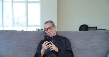 A senior citizen scrolling through his smartphone in the living room. (Shutterstock Photo)