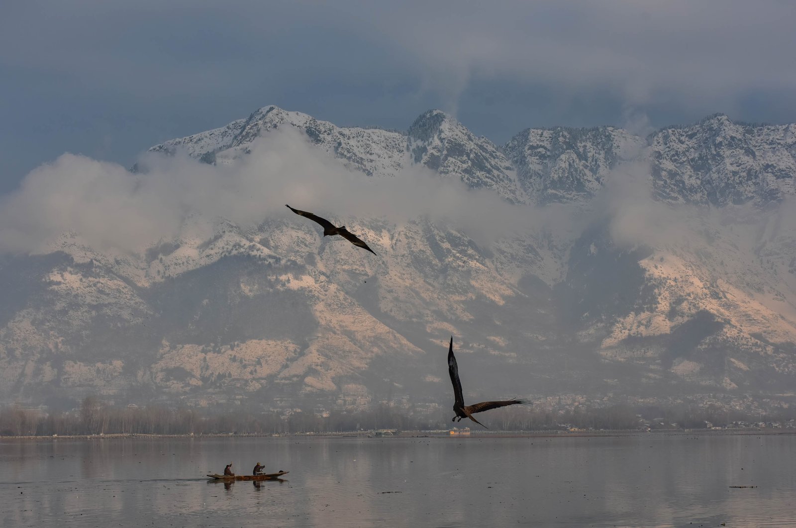A boat ferries a passenger across the Dal lake with snow-covered mountains in the background during a winter day after fresh snowfall in Srinagar, Jammu and Kashmir, Jan. 31, 2023. (Getty Images Photo)