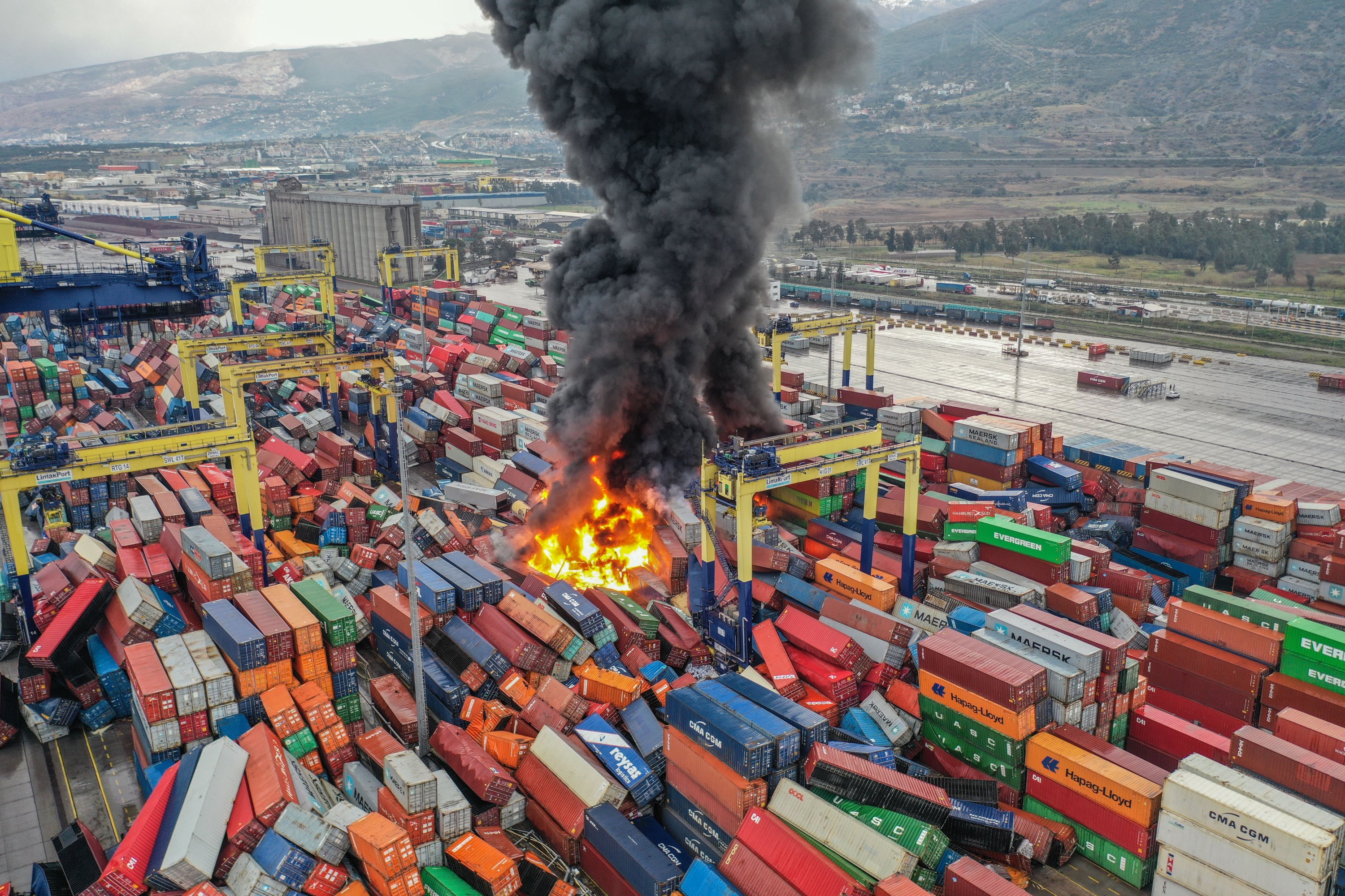 Asap gelap mengepul setelah kebakaran terjadi di antara kontainer yang terguling di pelabuhan utama di kota pesisir Mediterania Iskenderun setelah gempa bumi, Türkiye selatan, 6 Januari 2023. (Foto AA)