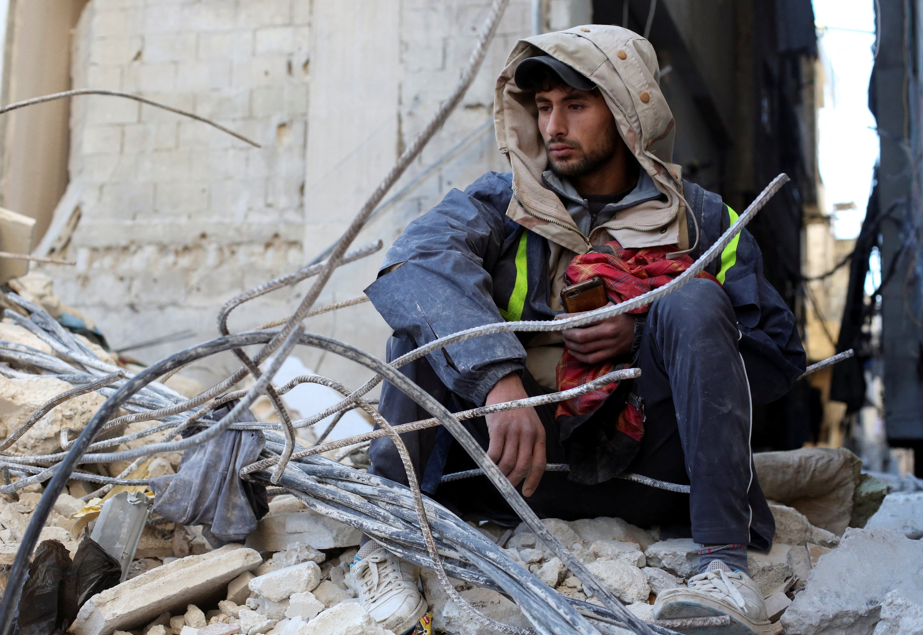 Seorang pria duduk di atas puing-puing bangunan yang rusak saat pencarian korban selamat berlanjut, Latakia, Suriah, 9 Februari 2023. (Foto Reuters)