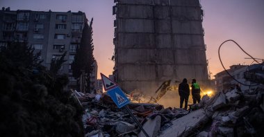 An excavator (rear) removes debris as two workers stand on the rubble at the site of collapsed buildings after a powerful earthquake, in Hatay, Feb. 13, 2023. (EPA Photo)
