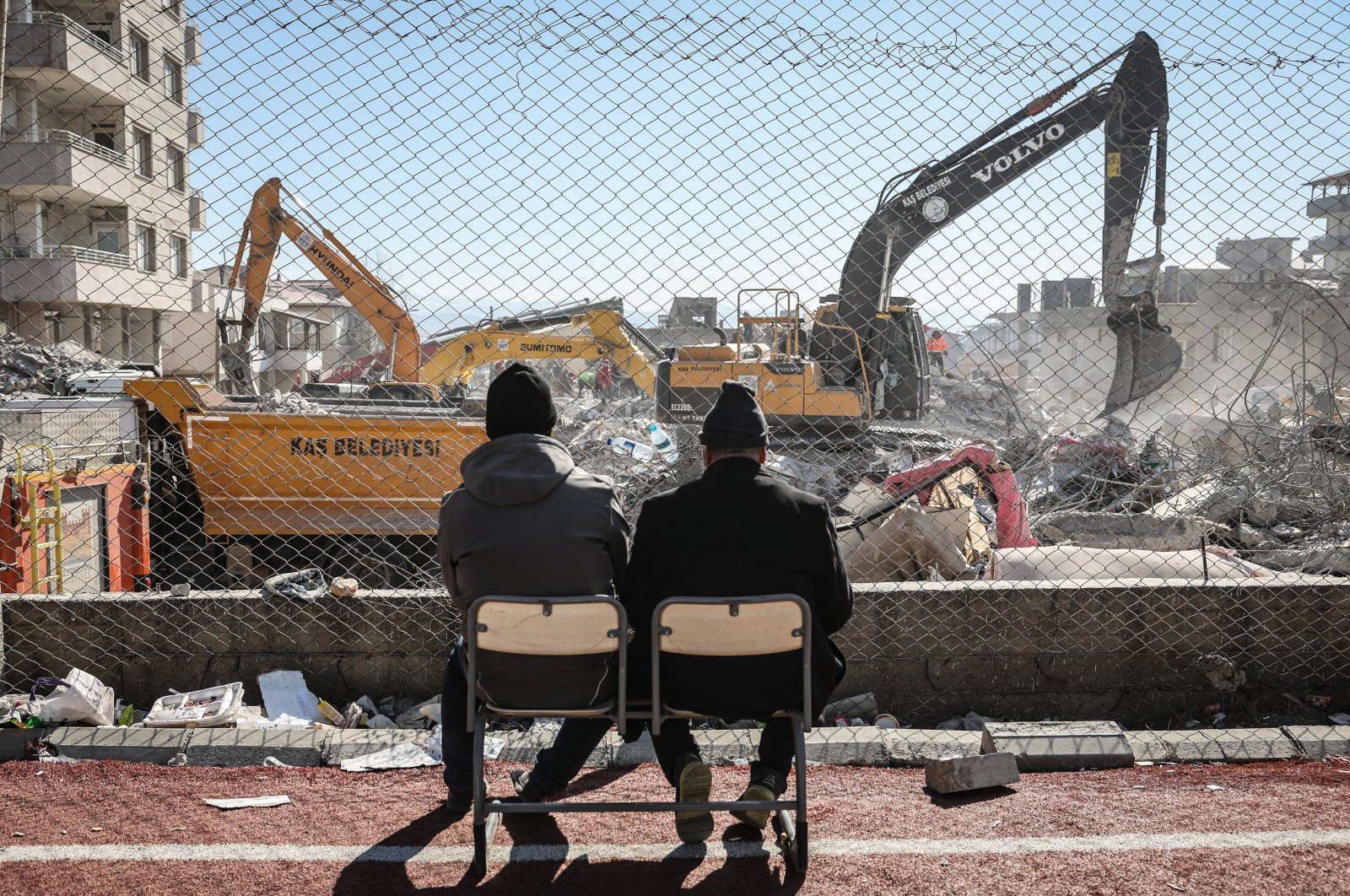 Two men watch excavators at work among the rubble of a collapsed building in the aftermath of an earthquake in Nurdaği, southeastern Türkiye, Feb. 13, 2023. (EPA Photo)