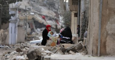 Syrian women and children sit wrapped in blankets outside collapsed buildings, Jandairis, Syria, Feb. 7, 2023. (AFP Photo)