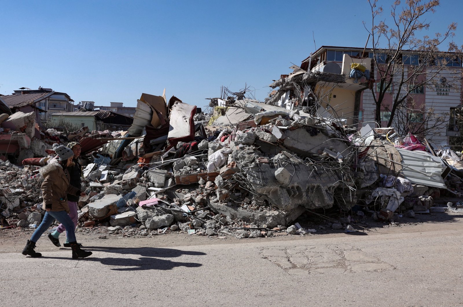 People walk past a collapsed building in the aftermath of the devastating earthquake in Nurdağı, Gaziantep, southeastern Türkiye, Feb. 13, 2023. (EPA Photo)