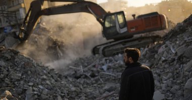 A Turkish man watches an excavator working in a destroyed building where he claims his fiancee is still under the rubble in Iskenderun city, Hatay, southern Türkiye, Feb. 14, 2023. (AP Photo)