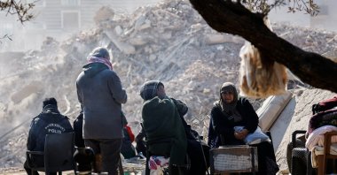 People sit at a camp next to the site of a destroyed high-end building, in the aftermath of the earthquake in Antakya, Hatay, southern Türkiye, Feb. 16, 2023. (Reuters Photo)