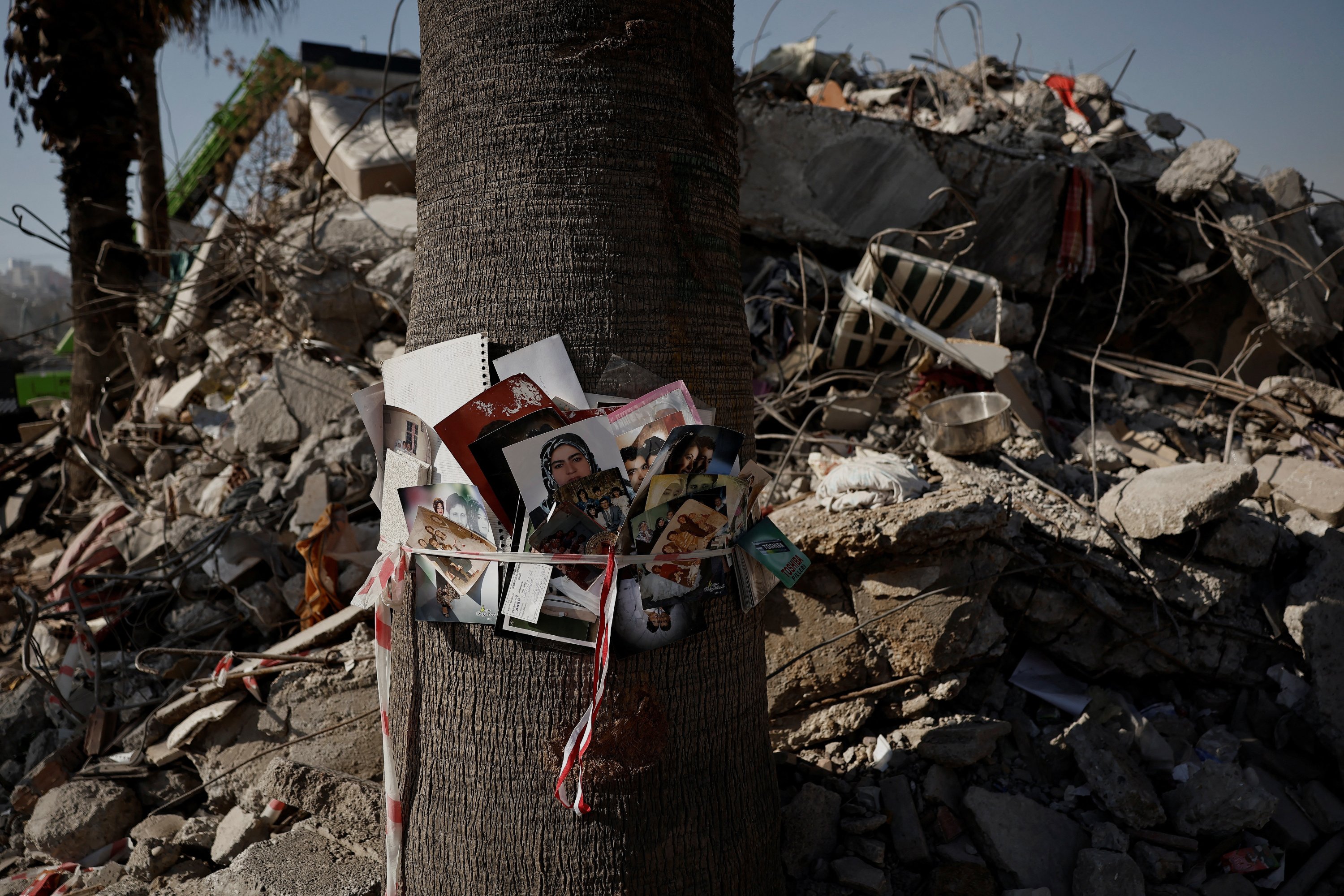 Foto-foto berbagai keluarga yang ditemukan di puing-puing bekas blok apartemen diikat ke batang pohon dengan pita polisi, setelah gempa mematikan, Kahramanmaraş, Türkiye, 18 Februari 2023. (Foto Reuters)