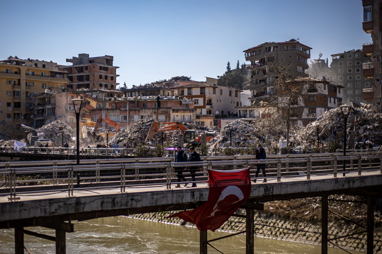 People walk on a bridge in front of collapsed buildings after a powerful earthquake, in Hatay, Türkiye, Feb. 17, 2023. (EPA Photo)