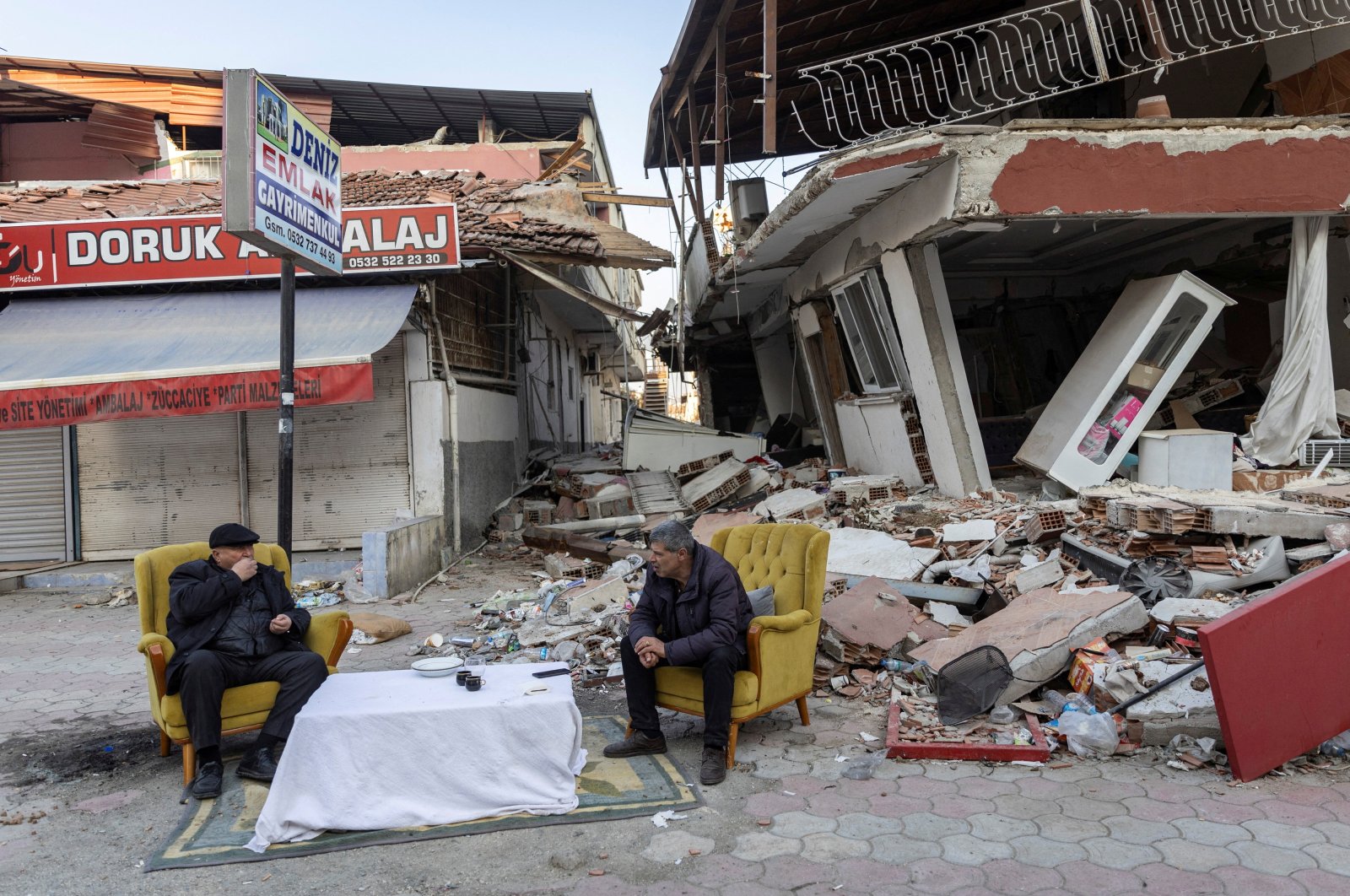 Men sit and talk in front of destroyed properties in the aftermath of the deadly earthquake in Antakya, Hatay province, Türkiye, Feb. 20, 2023. (Reuters Photo)