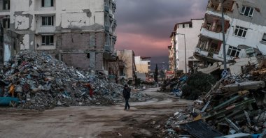 A man walks among collapsed buildings in earthquake-hit Samandağ district, in Hatay, southeastern Türkiye, Feb. 21, 2023. (AFP Photo)