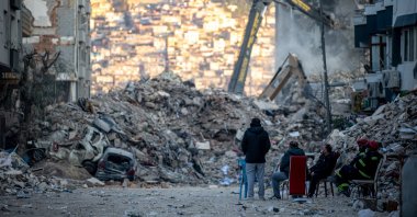 People sit in front of collapsed buildings after the deadly earthquake, in Hatay, southern Türkiye, Feb. 19, 2023. (EPA Photo)