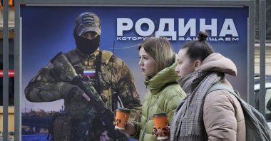 Girls walk past a stand with an image of a Russian serviceman and words 'The Motherland we defend' at a street exhibition of military photos in St. Petersburg, Russia, Feb. 9, 2023. (AP Photo)