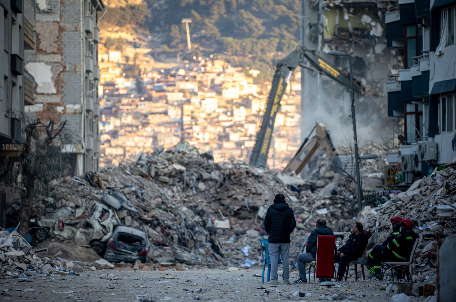 People sit in front of collapsed buildings after the deadly earthquake, in Hatay, southern Türkiye, Feb. 19, 2023. (EPA Photo)