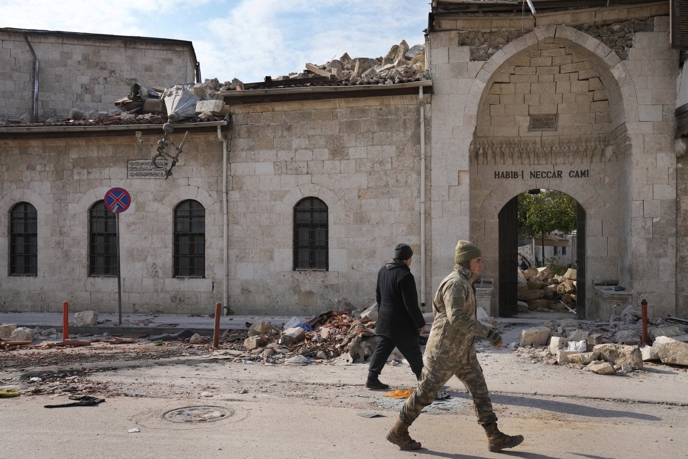 Bir Türk askeri, 11 Şubat 2023, Antakya'nın eski kentindeki büyük depremde yıkılan tarihi Habib Najjar camisinin ana girişinin önünden geçiyor. (AP Fotoğrafı)