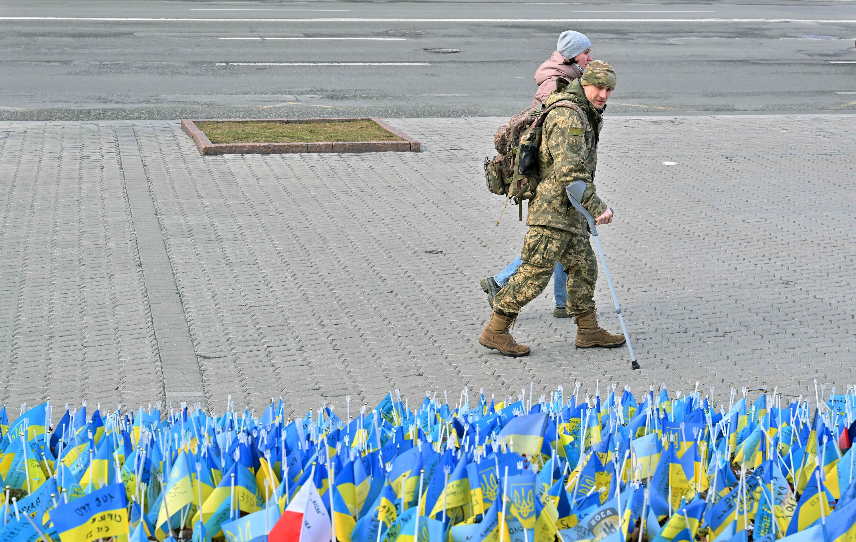 Seorang prajurit Ukraina yang terluka dan pacarnya berjalan melewati bendera nasional yang masing-masing melambangkan prajurit yang tewas, Kyiv, Ukraina, 22 Februari 2023. (Foto AFP)