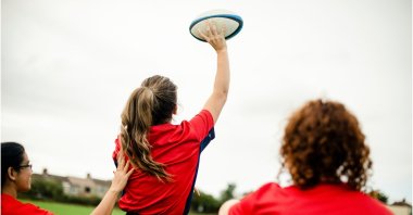 Woman playing rugby with teammates behind her. (Shutterstock Photo)