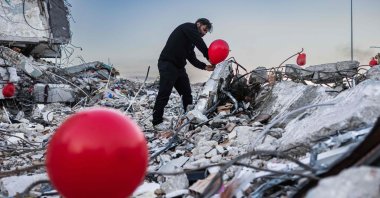 A Turkish man hangs balloons on the debris of a collapsed building, saying they are "the last toys" of children who died during the earthquake, Antakya, southern Türkiye, Feb. 21, 2023. (AFP Photo)
