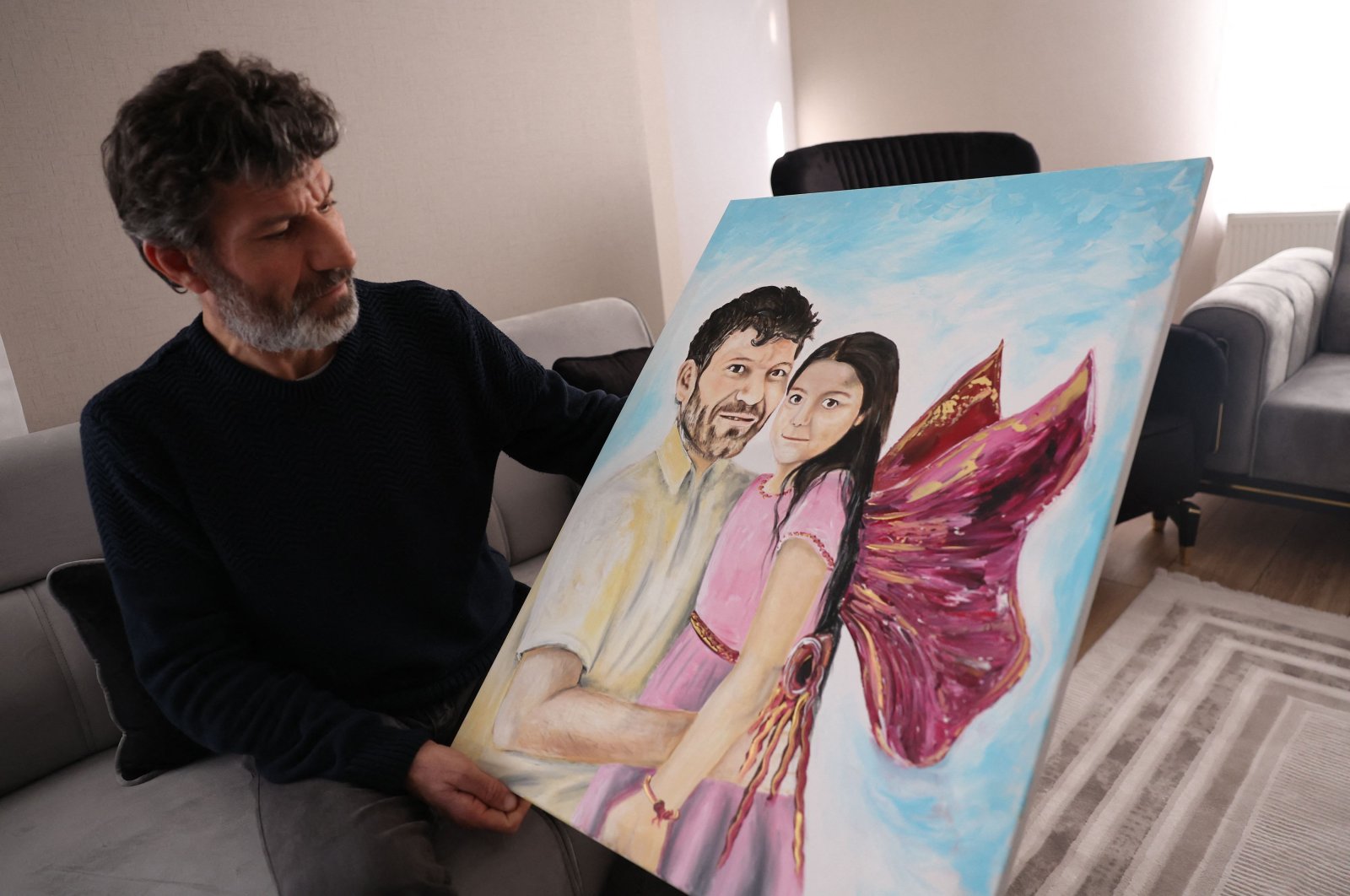 Turkish father Mesut Hançer, poses and holds a painting representing him and his daughter Irmak in his appartment as his family tries to rebuild, after losing their 15-years old daughter in the earthquake that devastated the southeastern region of Türkiye, Ankara, Türkiye, Feb. 25, 2023. (AFP Photo)