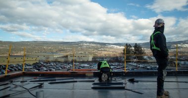 Workers install flat roofing as a plane passes overhead, at the childcare facility under construction at YLW Kelowna International Airport in Kelowna, British Columbia, Canada, Feb. 14, 2023. (Reuters Photo)