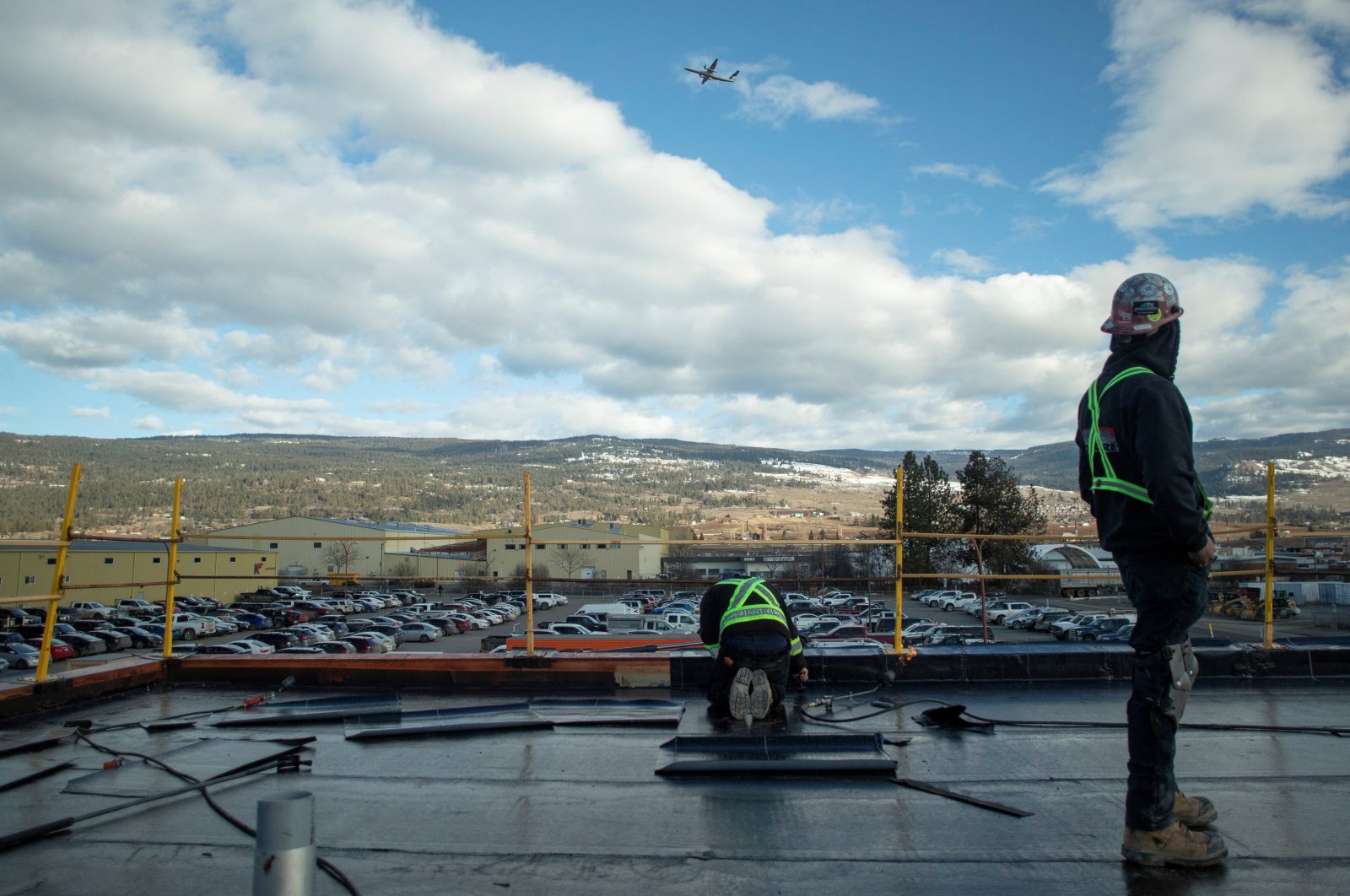 Workers install flat roofing as a plane passes overhead, at the childcare facility under construction at YLW Kelowna International Airport in Kelowna, British Columbia, Canada, Feb. 14, 2023. (Reuters Photo)