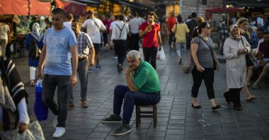 A man sits as people walk past by at the Spice Bazaar in Istanbul, Türkiye, Aug. 18, 2022. (AP Photo)