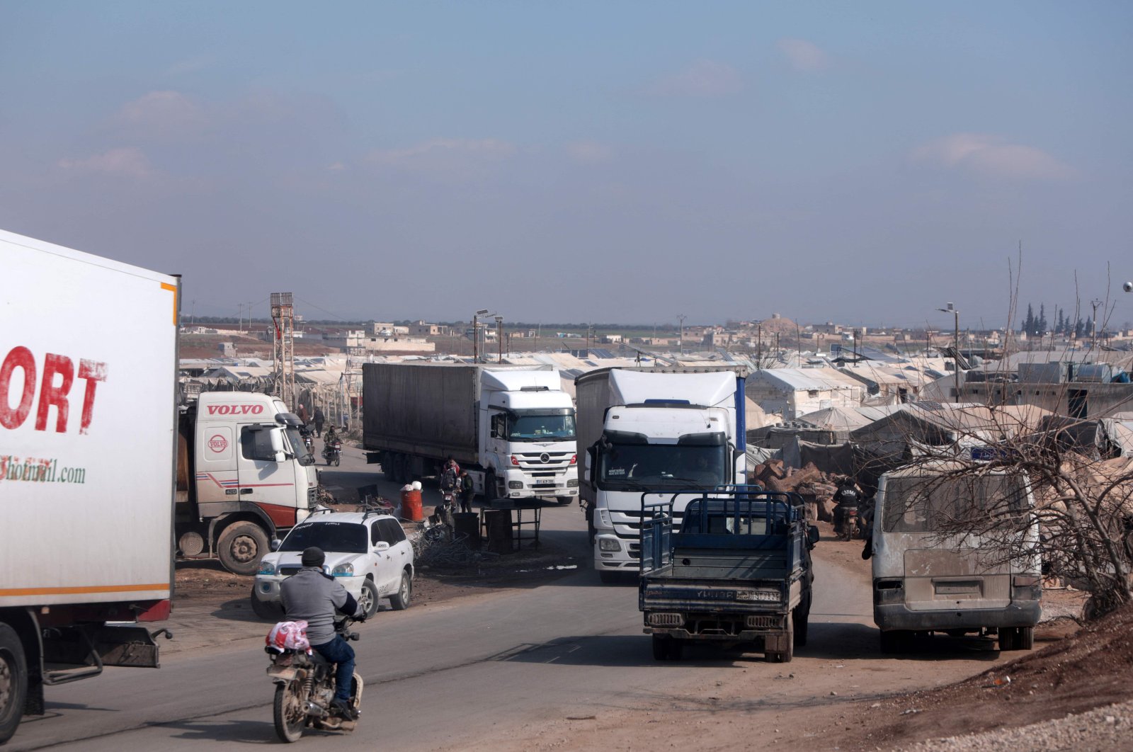 A convoy of trucks from Doctors Without Borders (MSF), carrying aid to earthquake victims, drives past tents sheltering survivors, after entering Syria from Türkiye via the al-Hamam border crossing in the countryside of Jindayris in northwestern Syria, on Feb.19, 2023. (AFP Photo)