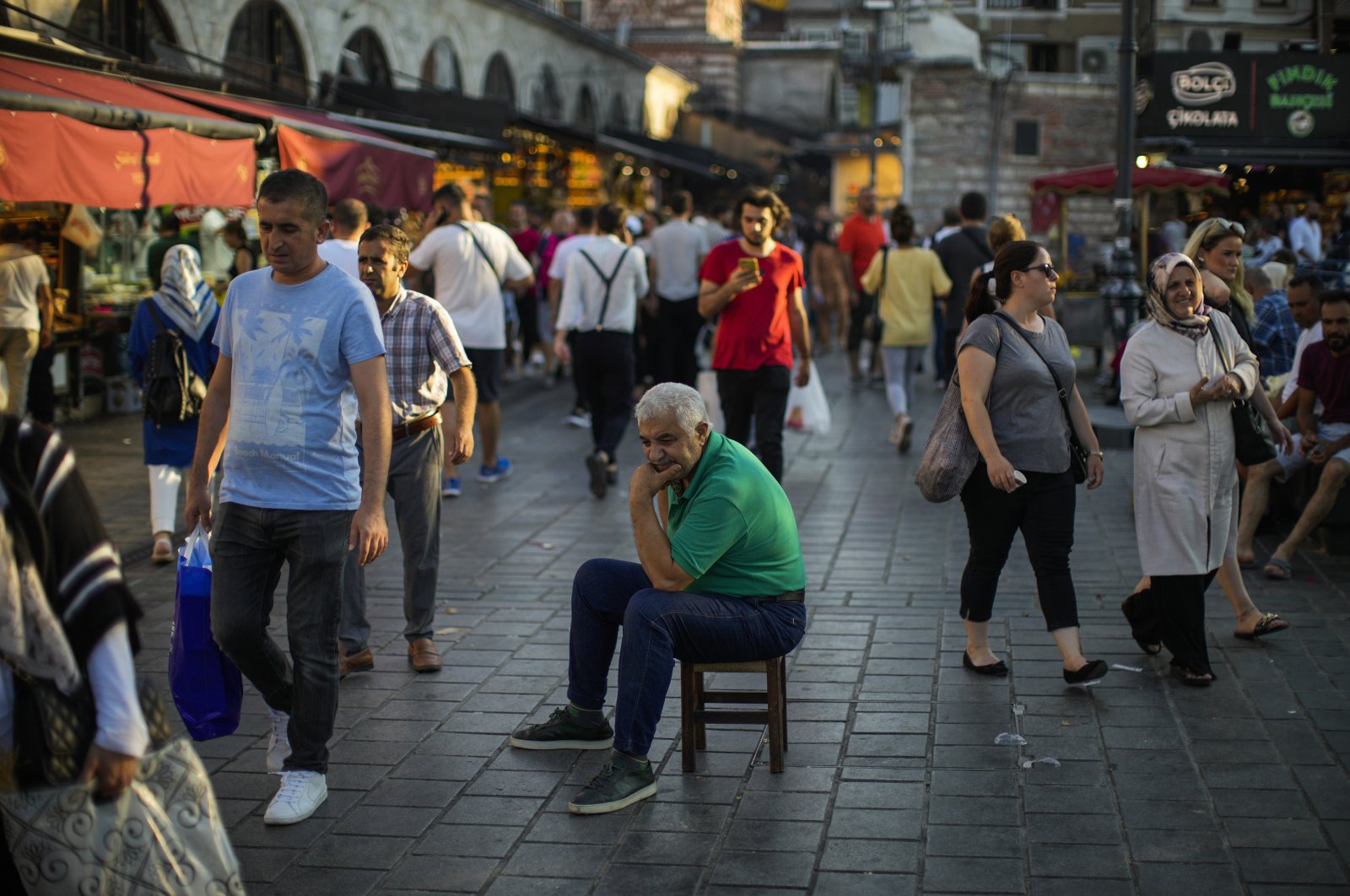 A man sits as people walk past by at the Spice Bazaar in Istanbul, Türkiye, Aug. 18, 2022. (AP Photo)