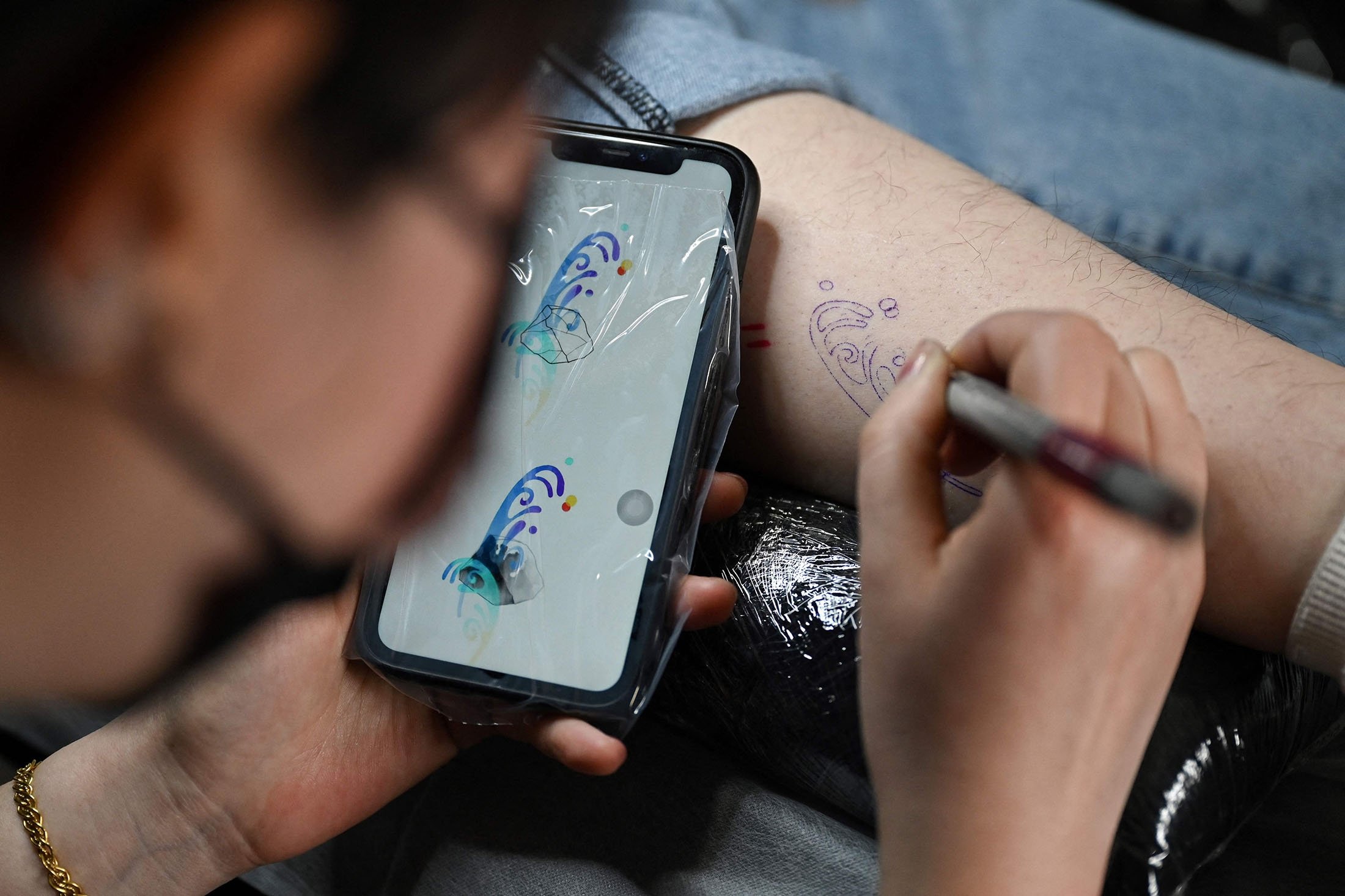 Seniman tato Tiongkok Song Jiayin membuat sketsa tato di kaki kliennya Liao Jingyi di studionya di Beijing, Tiongkok, 27 Februari 2023. (Foto AFP)