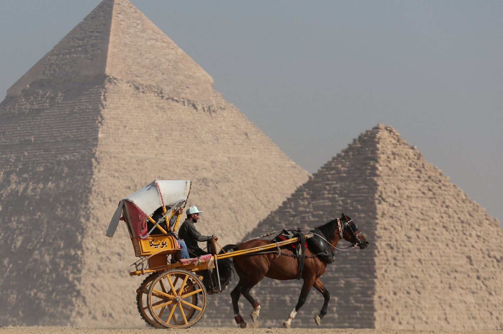 Tourists ride a horse-drawn cart in front of the Great Pyramids plateau in Giza, Egypt, Dec. 11, 2022. (Reuters Photo)