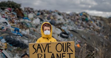 A child holding &#039;Save our Planet&#039; poster on landfill, environmental pollution, March 8, 2023. (Shutterstock Photo)