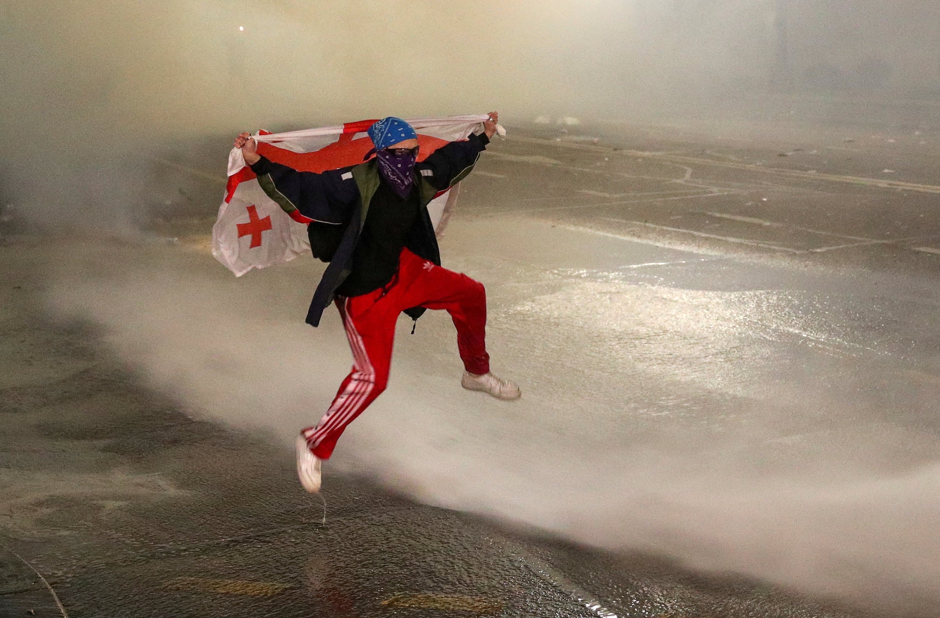 Seorang demonstran melompati semburan air saat protes di Tbilisi, Georgia, 9 Maret 2023. (Foto Reuters)