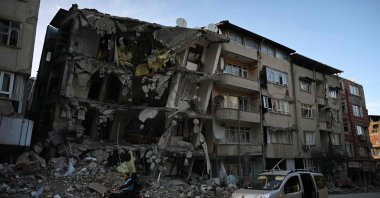 Two men ride a motorcycle in a destroyed neighborhood among the rubble of collapsed buildings in Hatay, on March 7, 2023. (AFP Photo)