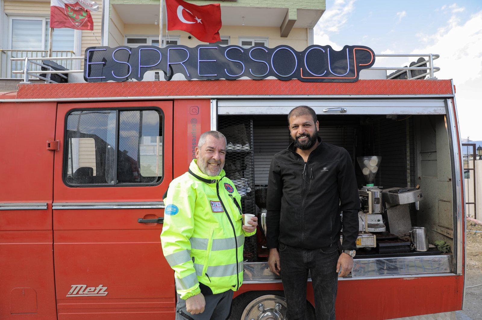 Mehmet Bağış (R) and a member of the Italian health team pose next to Bağış&#039;s espresso van in Hatay, southeastern Türkiye, March 10, 2023. (AA Photo)