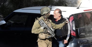 An Israeli soldier walks past a Palestinian man at the scene where three Palestinians were fatally shot in Nablus, occupied West Bank, March 12, 2023. (EPA Photo)