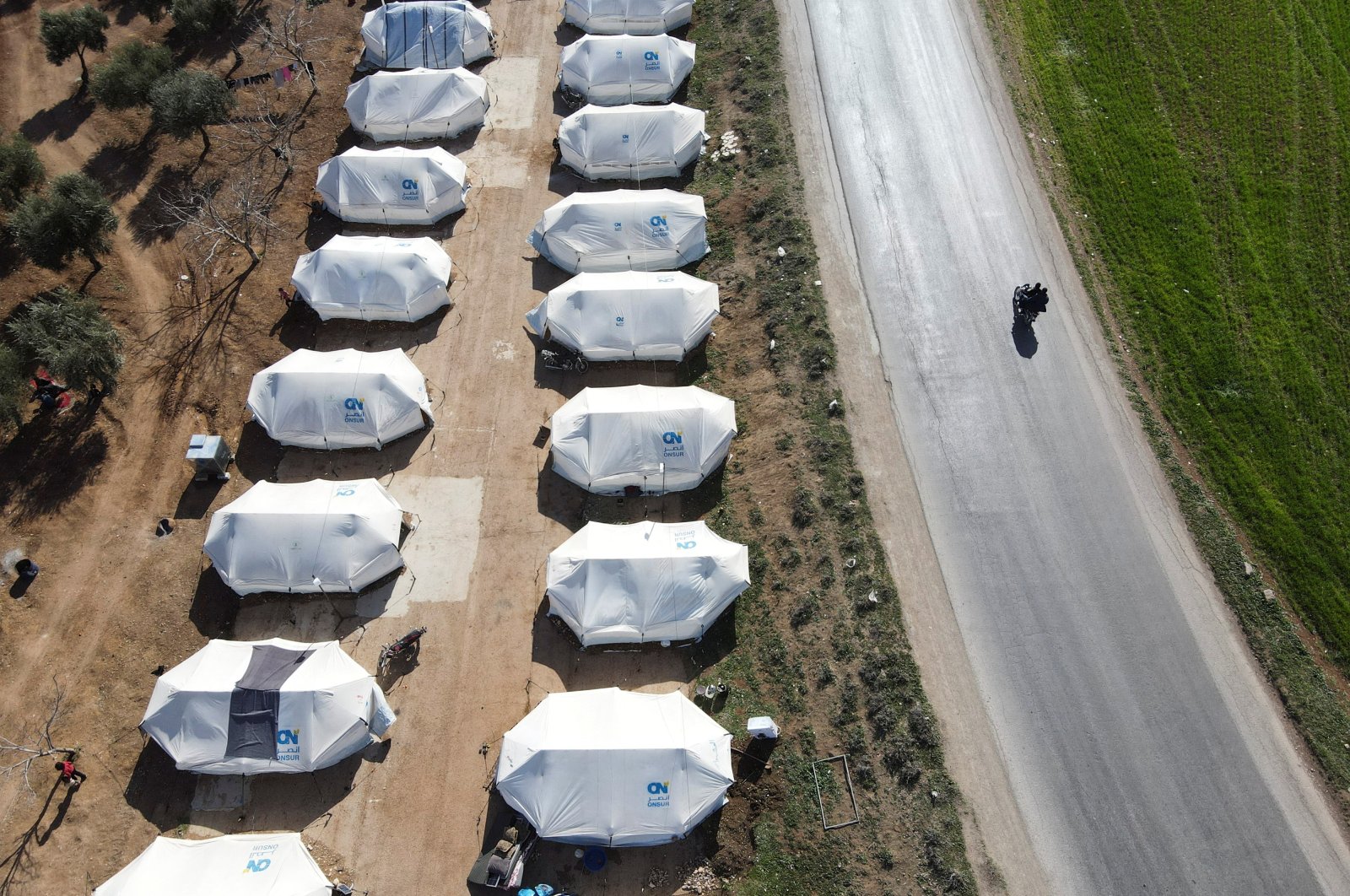 People ride on a motorbike past tents erected for the internally displaced following an earthquake, on a land that was previously a driving school, in the opposition-held town of Jandaris, Syria March 4, 2023. (Reuters Photo)