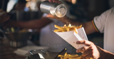 A man pours salt on french fries, in Milan, Italy. (Getty Images Photo)