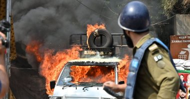A policeman stands near a burning vehicle during clashes with supporters of former PM Imran Khan, Lahore, March 15, 2023. (AFP Photo)