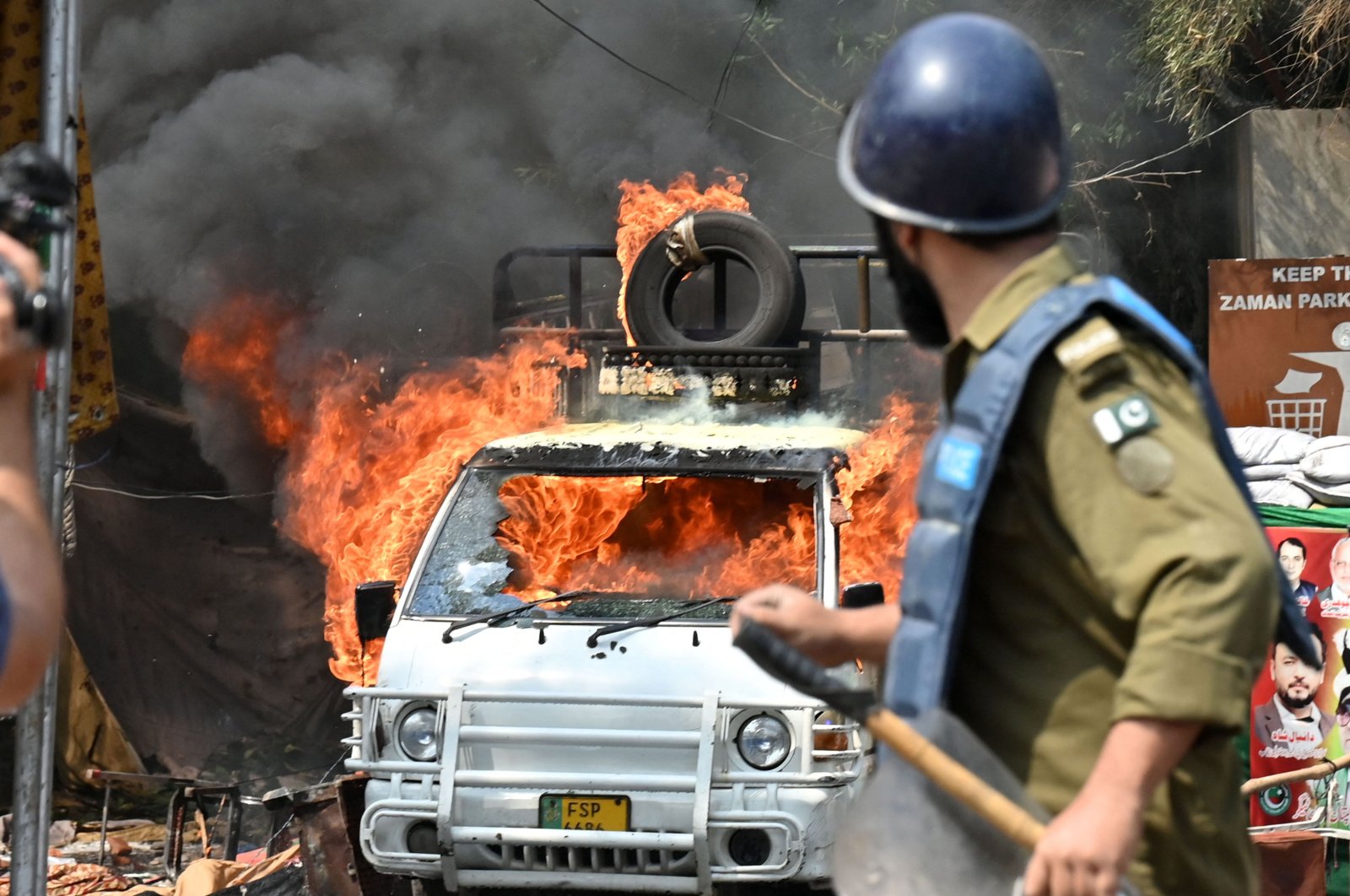 A policeman stands near a burning vehicle during clashes with supporters of former PM Imran Khan, Lahore, March 15, 2023. (AFP Photo)