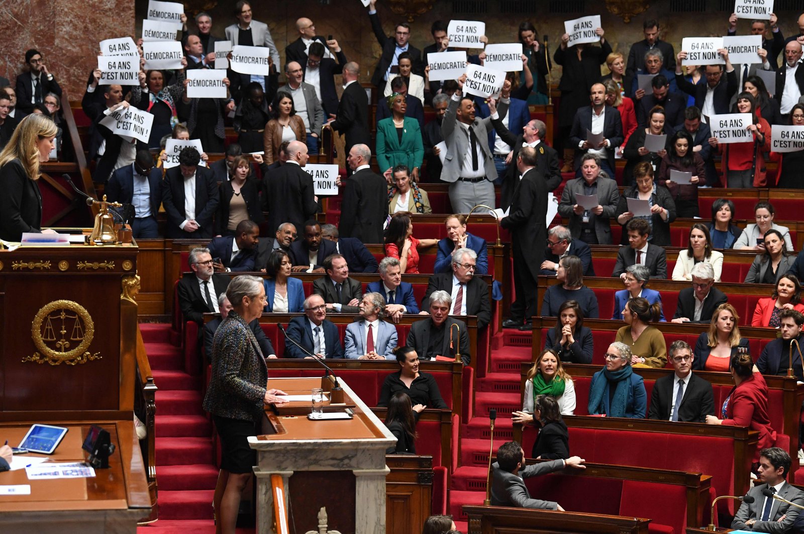 Members of Parliament of left-wing coalition NUPES (New People&#039;s Ecologic and Social Union) hold placards during the speech of France&#039;s Prime Minister Elisabeth Borne (center), as she confirms to force through pension law without parliament vote during a session on the government&#039;s pension reform at the lower house National Assembly, in Paris, France, March 16, 2023. (AFP Photo)