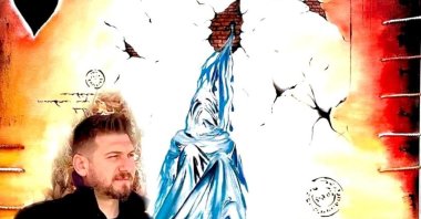 Surrealist painter Vahap Aydoğan stands near his artwork. (Photo courtesy of the artist)