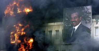 A portrait of Saddam Hussein still hangs on the burning Ministry of Transport and Communication building in Baghdad, April 9, 2003. (AP Photo)