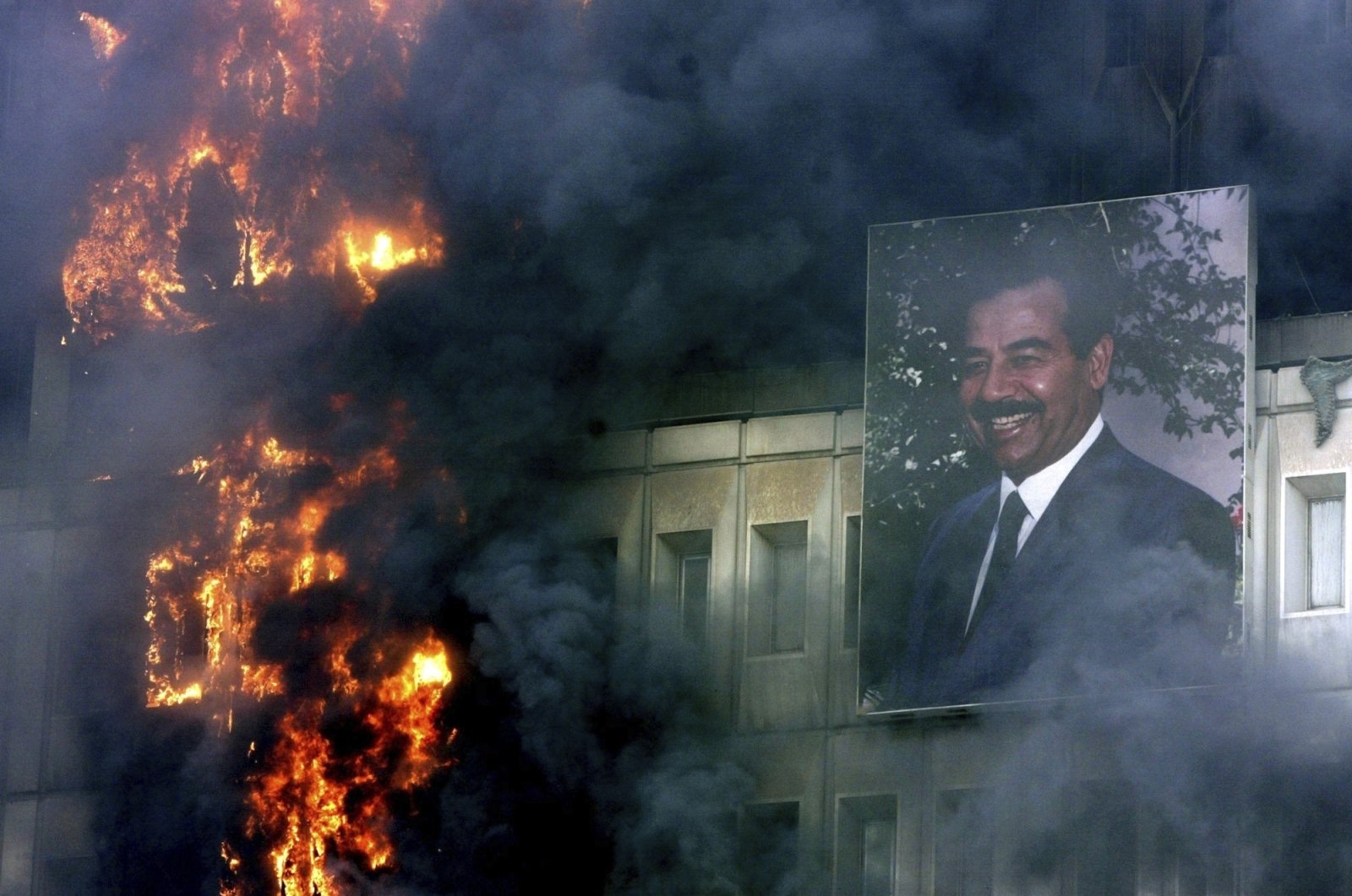 A portrait of Saddam Hussein still hangs on the burning Ministry of Transport and Communication building in Baghdad, April 9, 2003. (AP Photo)