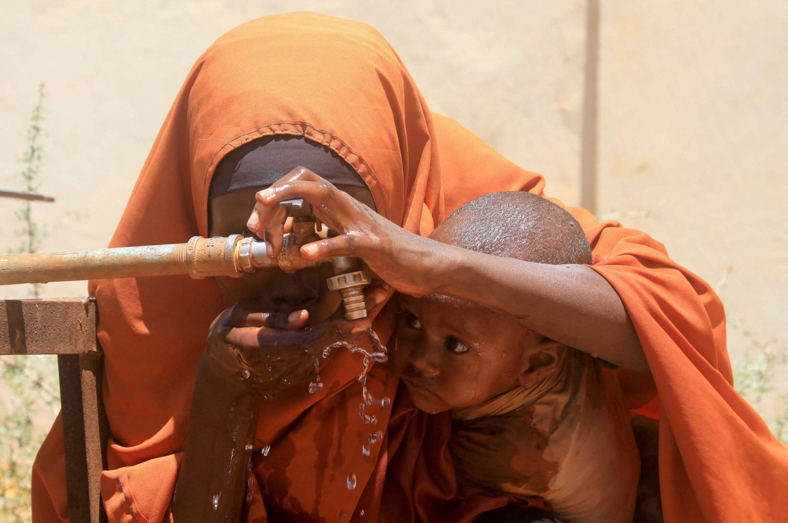 A Somali woman holds her child as they drink water outside the feeding center, Barwaaqo, near Baidoa, Somalia, Feb. 21, 2023. (Reuters Photo)