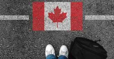 A man stands on the asphalt next to a flag of Canada near the country's border with the U.S.