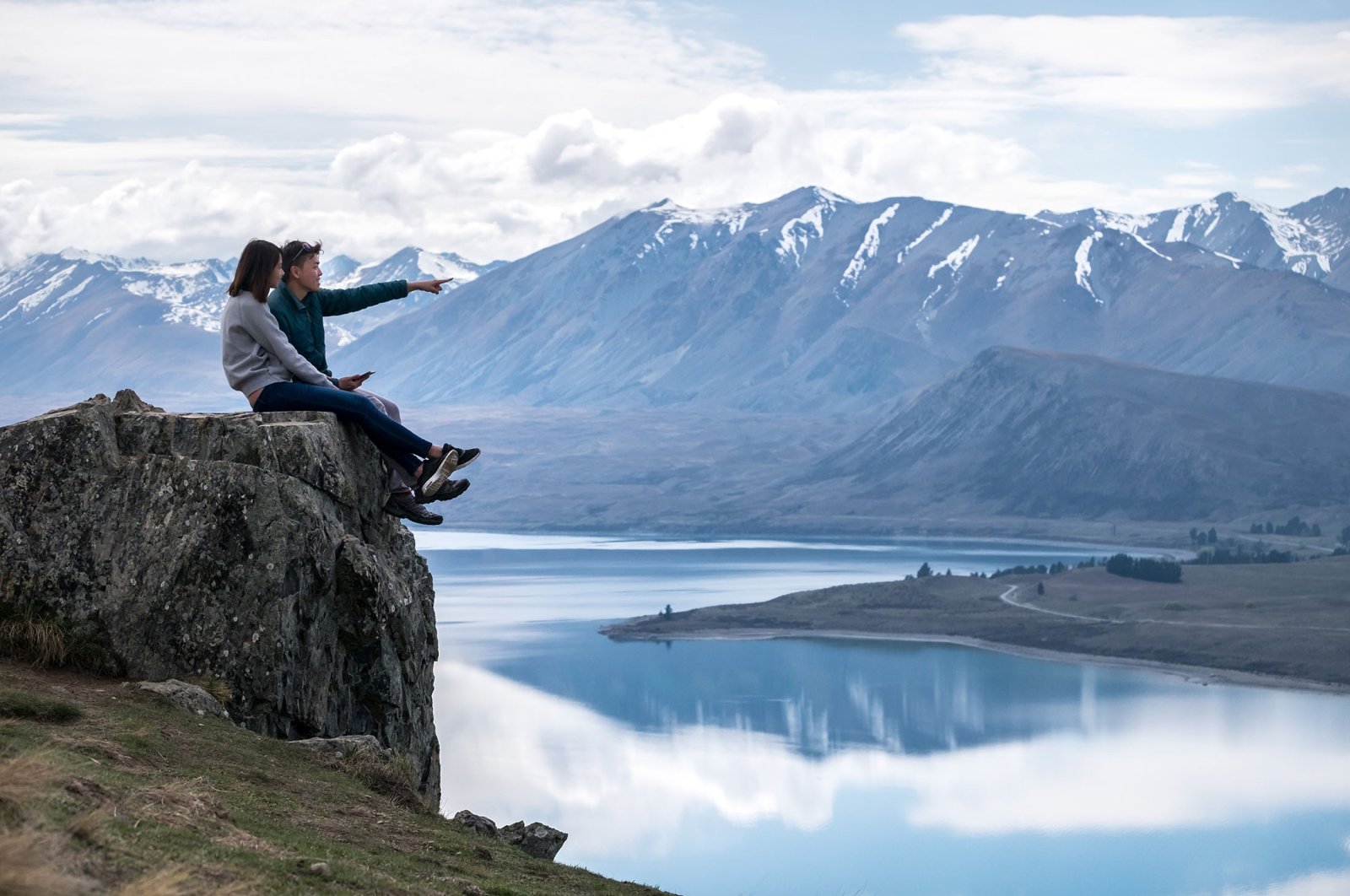 A young couple sits on a rock in New Zealand. (Shutterstock Photo)