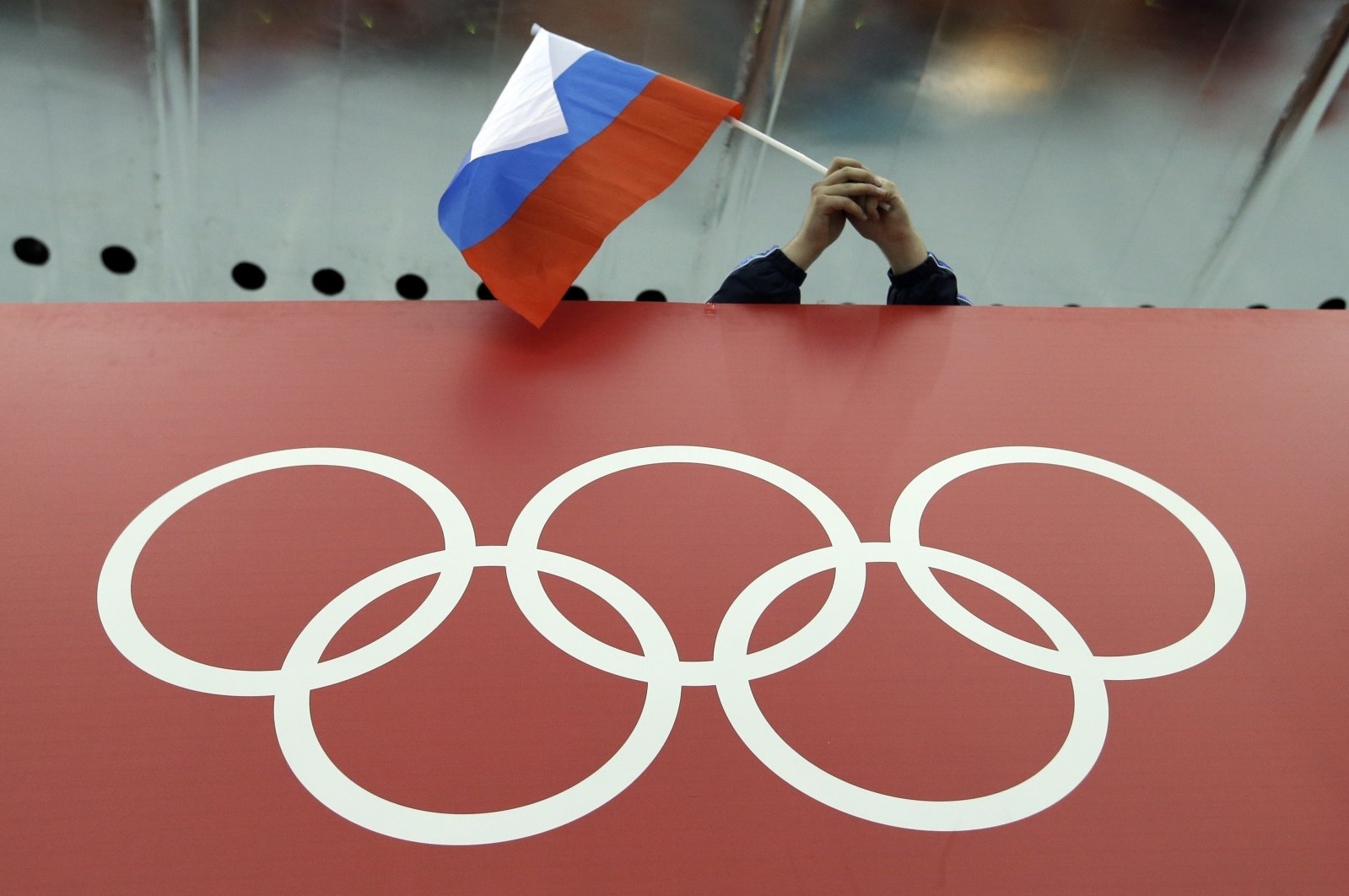 A Russian flag is held above the Olympic Rings at Adler Arena Skating Center during the Winter Olympics in Sochi, Russia, Feb. 18, 2014. (AP Photo)