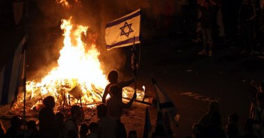 Protesters hold an Israeli flag as they gather around a bonfire during an anti-government rally, Tel Aviv, Israel, March 27, 2023. (AFP Photo)